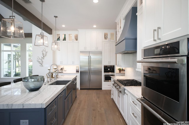 kitchen with light stone counters, stainless steel appliances, custom exhaust hood, and white cabinets