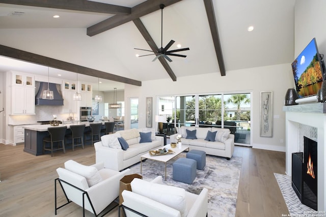 living room with beamed ceiling, high vaulted ceiling, a high end fireplace, and light hardwood / wood-style flooring