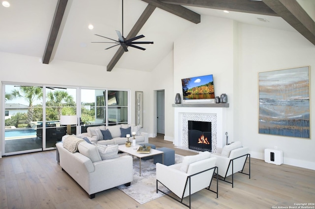 living room featuring light hardwood / wood-style flooring, ceiling fan, beam ceiling, high vaulted ceiling, and a tiled fireplace