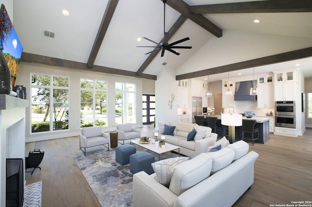 living room featuring high vaulted ceiling, sink, light wood-type flooring, ceiling fan, and beam ceiling