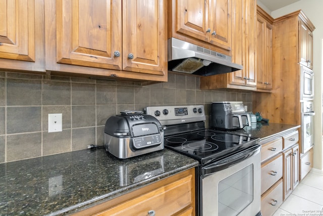 kitchen with dark stone countertops, backsplash, appliances with stainless steel finishes, and light tile patterned flooring