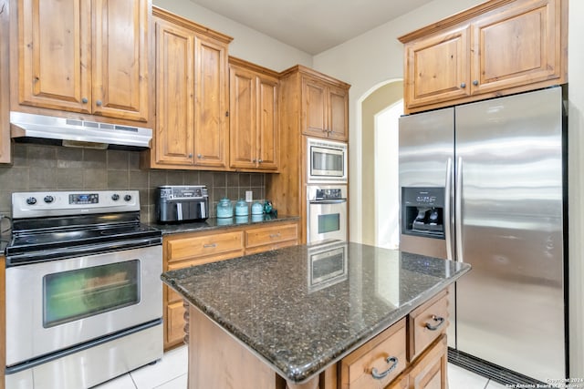 kitchen featuring a kitchen island, backsplash, dark stone countertops, light tile patterned floors, and appliances with stainless steel finishes