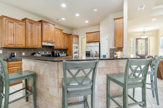 kitchen with kitchen peninsula, hanging light fixtures, backsplash, appliances with stainless steel finishes, and a breakfast bar area