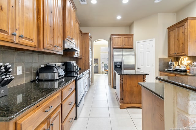 kitchen featuring a kitchen island, backsplash, dark stone countertops, range with electric stovetop, and light tile patterned floors