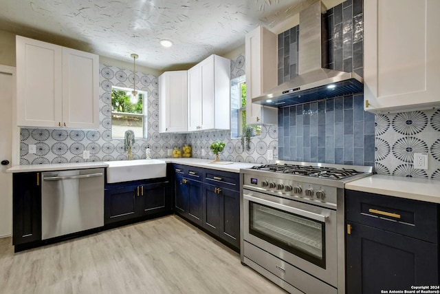 kitchen with wall chimney exhaust hood, light hardwood / wood-style flooring, stainless steel appliances, pendant lighting, and white cabinetry