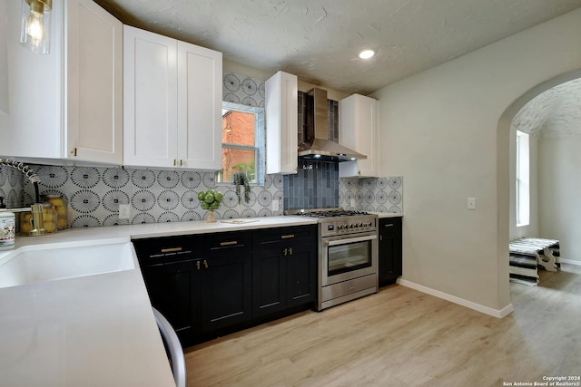 kitchen featuring stainless steel gas range oven, wall chimney exhaust hood, arched walkways, white cabinets, and dark cabinets