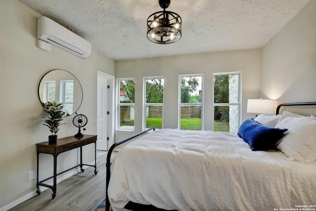 bedroom featuring an inviting chandelier, baseboards, a wall unit AC, and wood finished floors
