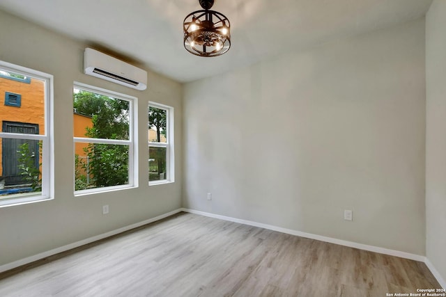 unfurnished room featuring a chandelier, a wall mounted AC, baseboards, and wood finished floors