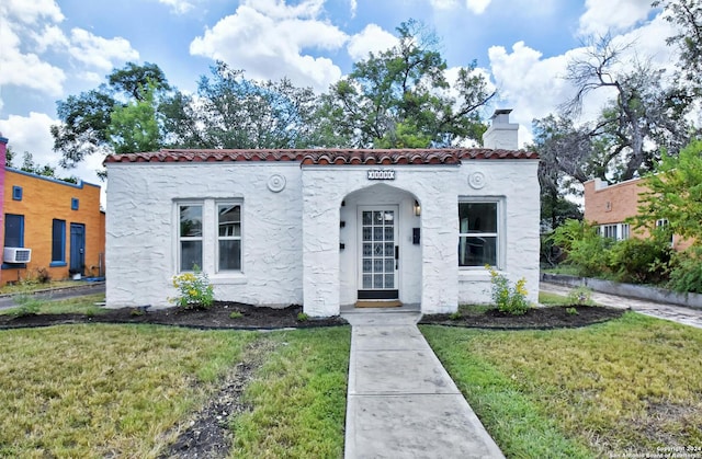 mediterranean / spanish house featuring a tiled roof, stucco siding, a chimney, and a front yard