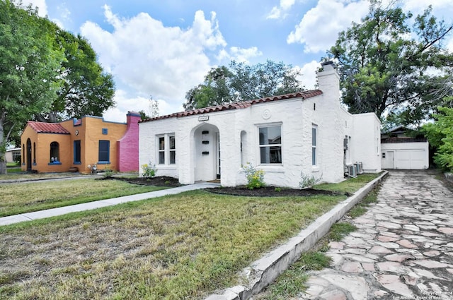 mediterranean / spanish home with a front lawn, a tiled roof, stucco siding, and central AC unit