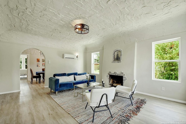 living room with light wood-type flooring, a fireplace, a wall mounted AC, and arched walkways