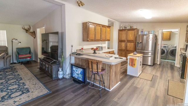 kitchen featuring lofted ceiling, kitchen peninsula, stainless steel fridge, a kitchen bar, and a textured ceiling