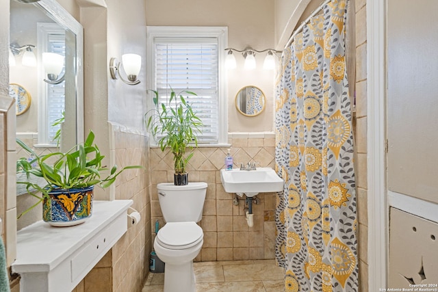 bathroom with toilet, tile patterned floors, tile walls, and sink