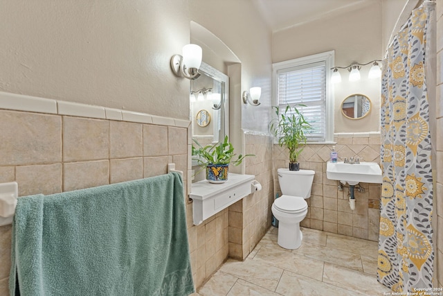 bathroom with toilet, sink, and tile walls