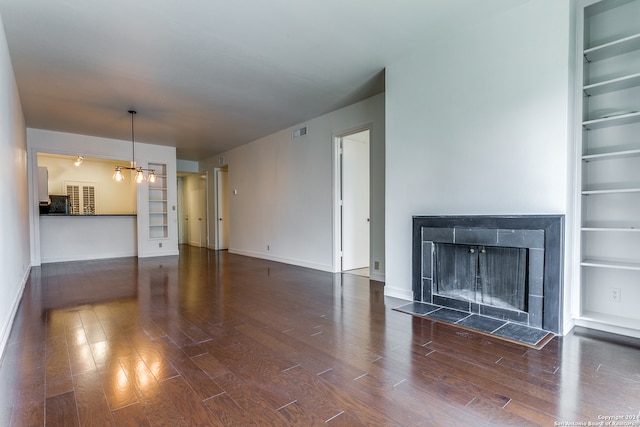 unfurnished living room with dark wood-type flooring, a tiled fireplace, and a notable chandelier