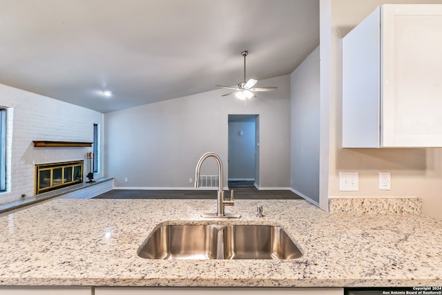 kitchen with ceiling fan, light stone countertops, a brick fireplace, vaulted ceiling, and sink