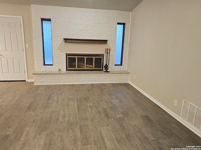 unfurnished living room featuring hardwood / wood-style flooring and a brick fireplace