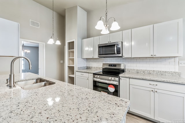 kitchen featuring white cabinetry, stainless steel appliances, sink, decorative light fixtures, and light stone counters