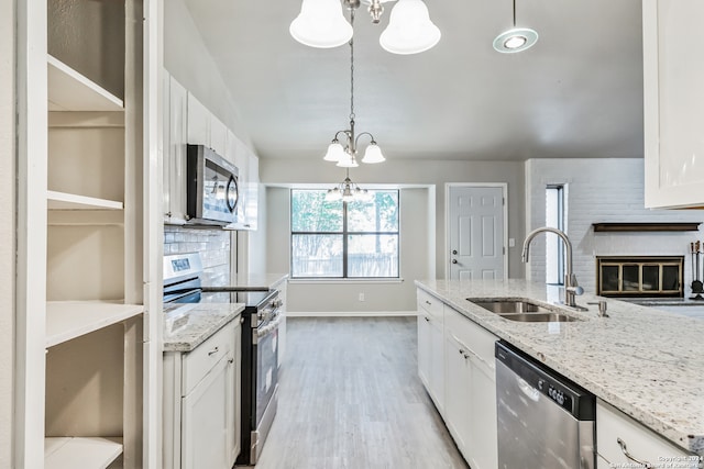 kitchen featuring light stone countertops, sink, white cabinetry, stainless steel appliances, and decorative light fixtures