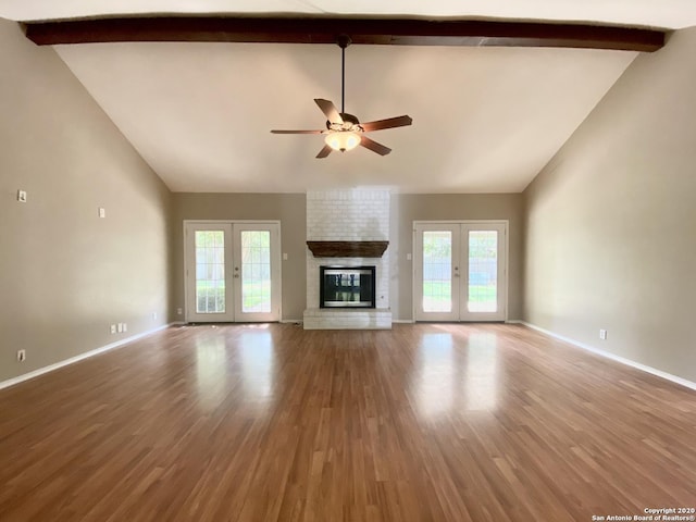 unfurnished living room with a ceiling fan, high vaulted ceiling, beamed ceiling, a brick fireplace, and french doors