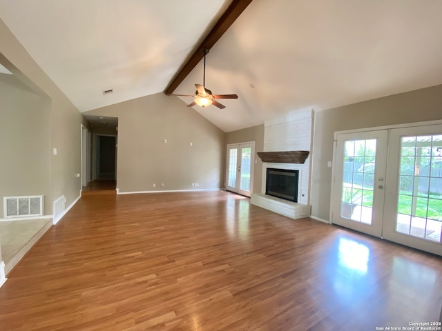 unfurnished living room featuring a large fireplace, ceiling fan, vaulted ceiling with beams, light hardwood / wood-style floors, and french doors