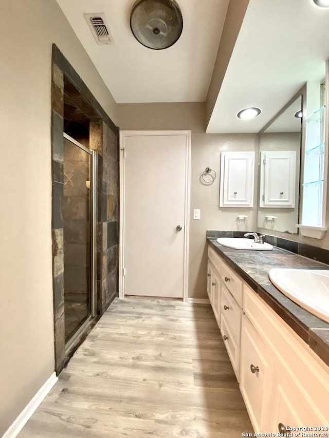 full bath with a shower stall, wood finished floors, baseboards, and double vanity