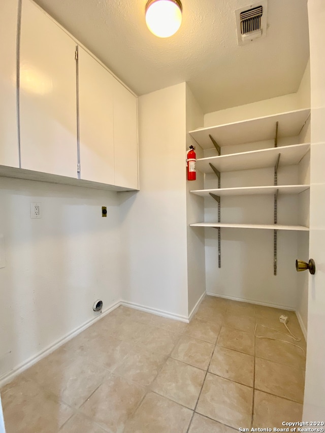 washroom featuring hookup for an electric dryer, a textured ceiling, light tile patterned floors, and cabinets