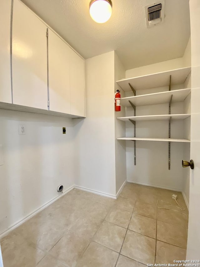 laundry room featuring electric dryer hookup, cabinet space, light tile patterned floors, baseboards, and a textured ceiling