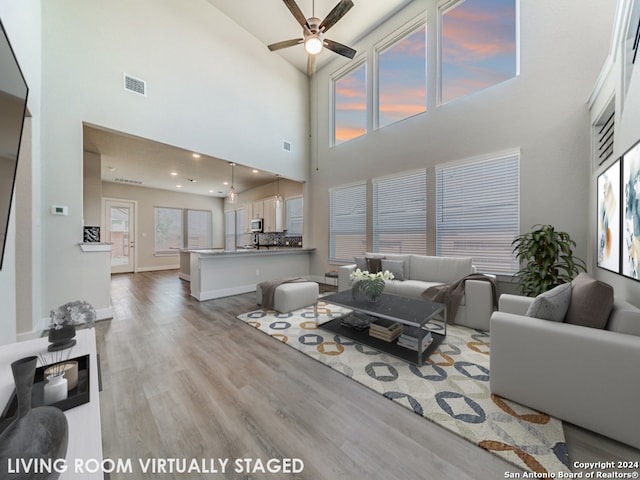 living room with ceiling fan, light wood-type flooring, a towering ceiling, and plenty of natural light