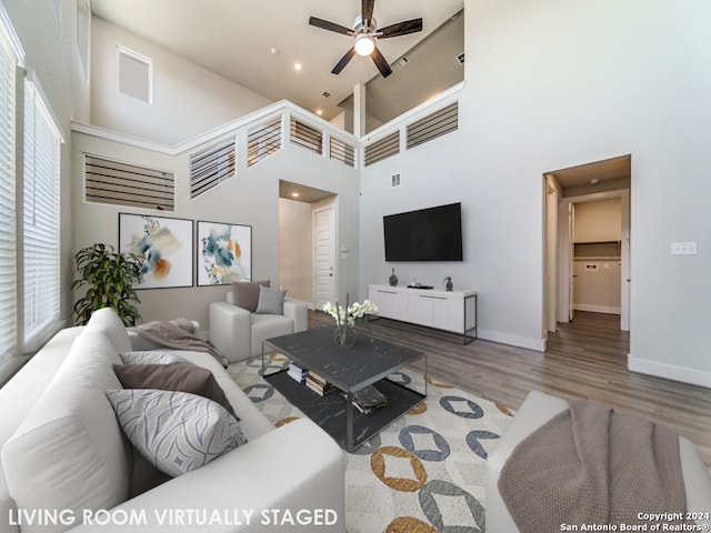 living room with ceiling fan, a towering ceiling, and wood-type flooring