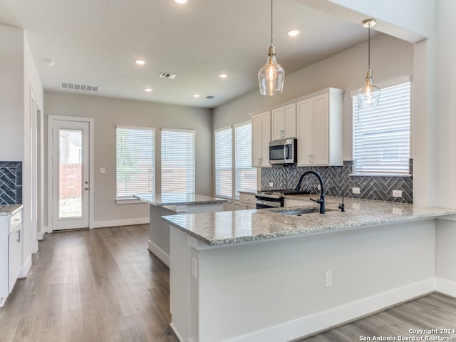 kitchen with kitchen peninsula, hanging light fixtures, appliances with stainless steel finishes, white cabinetry, and light stone counters