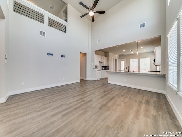 unfurnished living room featuring a towering ceiling, ceiling fan, light hardwood / wood-style floors, and a wealth of natural light