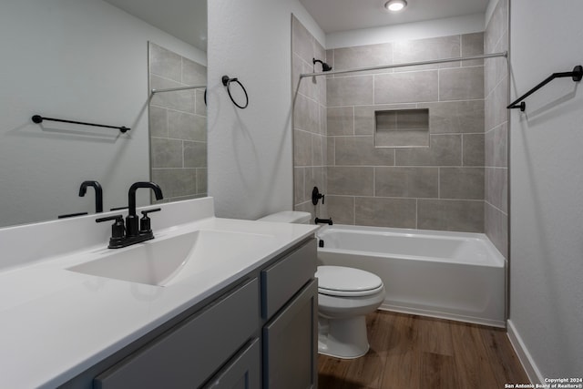 full bathroom with hardwood / wood-style floors, tiled shower / bath combo, vanity, and toilet