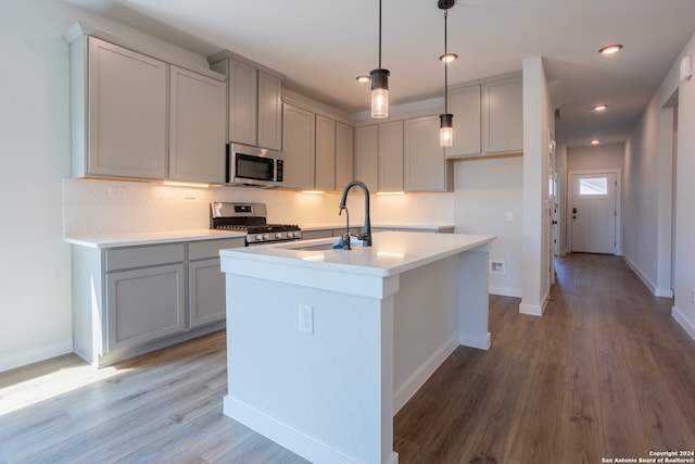 kitchen with gray cabinetry, appliances with stainless steel finishes, sink, hardwood / wood-style flooring, and a kitchen island with sink