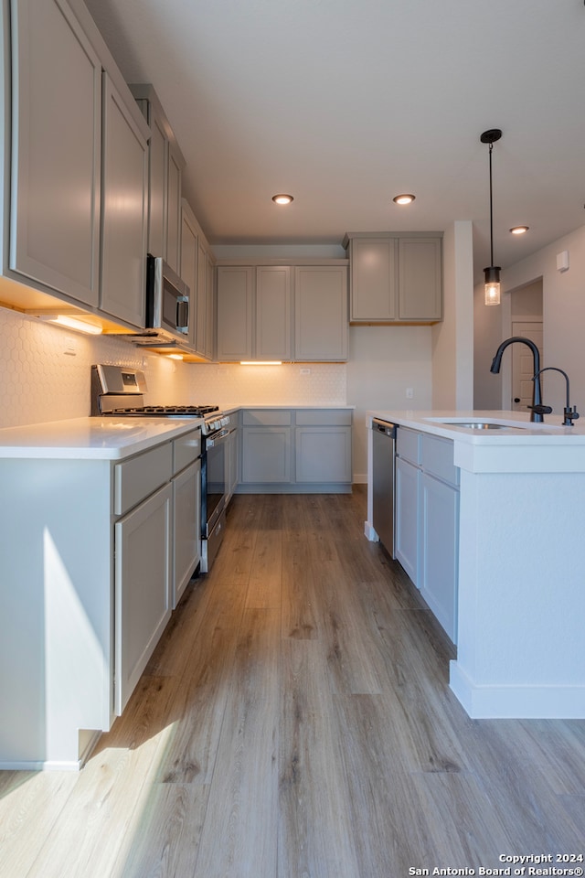 kitchen featuring light hardwood / wood-style floors, gray cabinets, appliances with stainless steel finishes, decorative light fixtures, and sink