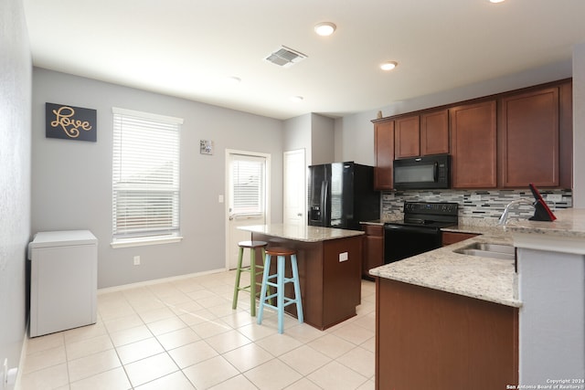 kitchen with a kitchen island, a breakfast bar area, black appliances, light stone counters, and tasteful backsplash