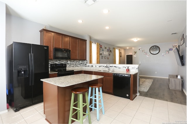 kitchen with tasteful backsplash, black appliances, sink, a kitchen island, and a breakfast bar