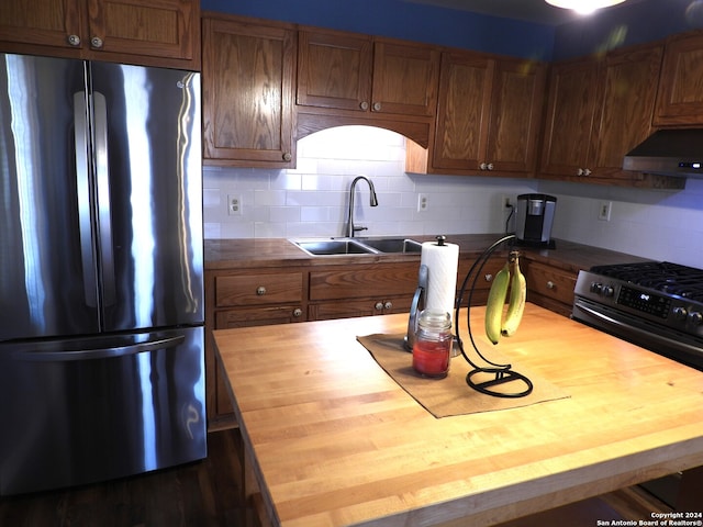 kitchen with tasteful backsplash, sink, butcher block countertops, extractor fan, and stainless steel refrigerator