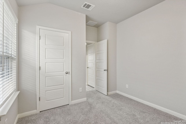 unfurnished bedroom with lofted ceiling, multiple windows, and light colored carpet