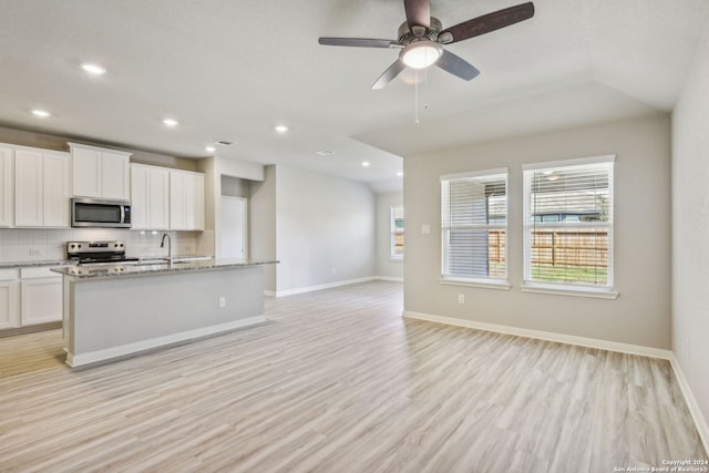 kitchen with white cabinets, a center island with sink, light stone countertops, light wood-type flooring, and stainless steel appliances