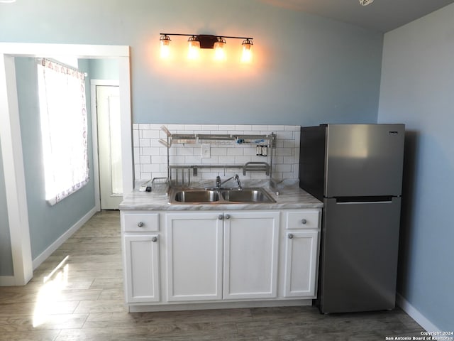 kitchen featuring tasteful backsplash, white cabinetry, stainless steel refrigerator, light hardwood / wood-style floors, and sink