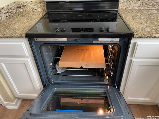 details featuring black range with electric cooktop, wood-type flooring, and white cabinets