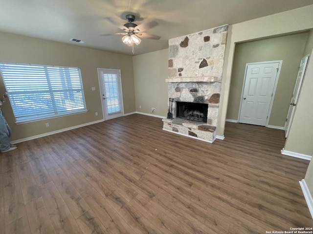 unfurnished living room with a stone fireplace, ceiling fan, and dark hardwood / wood-style flooring