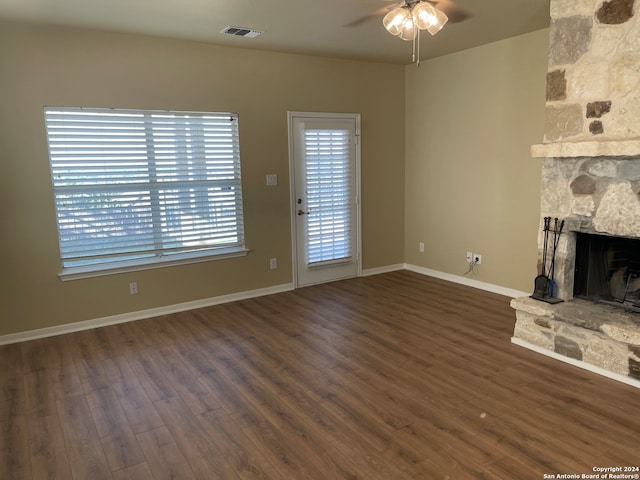 unfurnished living room with dark wood-type flooring, ceiling fan, and a stone fireplace