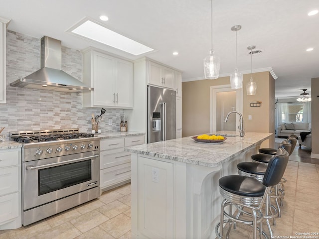 kitchen with white cabinetry, premium appliances, wall chimney exhaust hood, and an island with sink