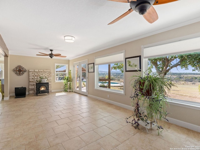 unfurnished living room featuring ceiling fan, a wood stove, ornamental molding, and light tile patterned floors