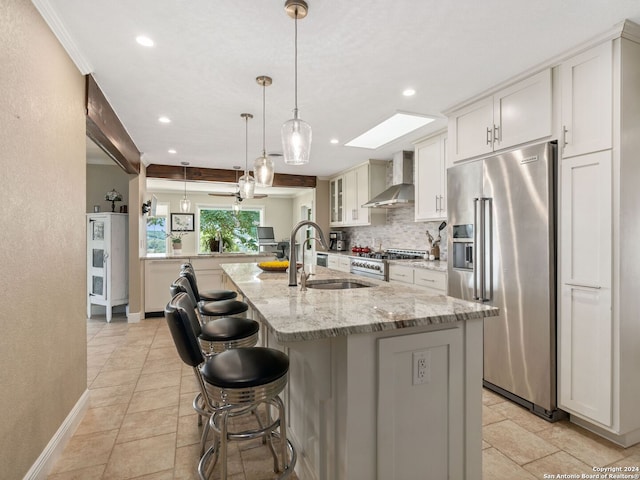 kitchen with wall chimney range hood, white cabinets, a center island with sink, sink, and premium appliances