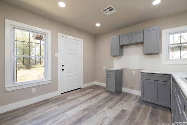 kitchen featuring gray cabinetry, tasteful backsplash, light stone countertops, and light wood-type flooring