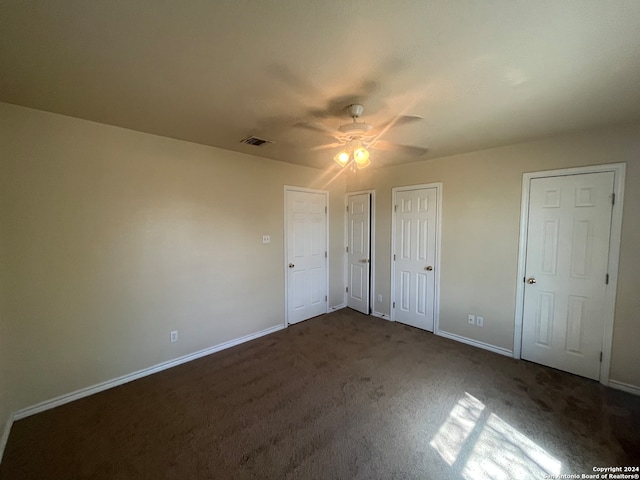 unfurnished bedroom featuring multiple closets, dark colored carpet, and ceiling fan