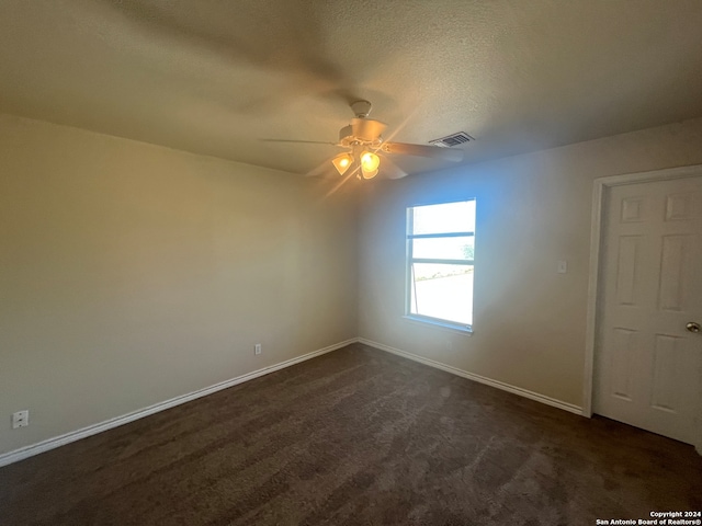 empty room featuring ceiling fan, a textured ceiling, and dark colored carpet